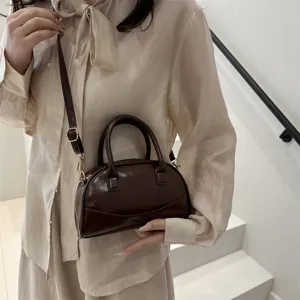 Close-up detail of a stylish dark brown Boston handbag with top handles and a chic crossbody strap.