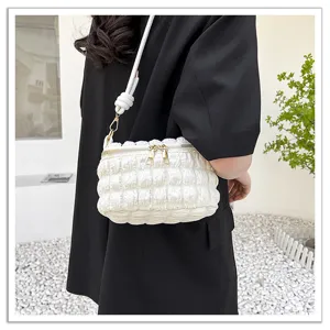 Detailed shot of white quilted crinkle shoulder bag with knotted strap and golden zippers.