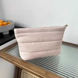 Pink quilted puffer cosmetic bag detail view, soft fabric makeup pouch with gold zipper.