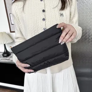 Detailed view of the black quilted clutch bag, showing soft padded texture and golden zip.
