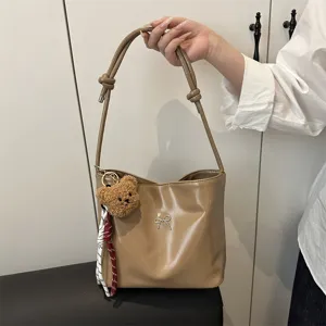 Detailed view of the brown glossy shoulder bucket bag with a cute bear pendant and bow.