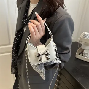 Detail view of mini white crossbody bag featuring silver bow and chain strap for kids.
