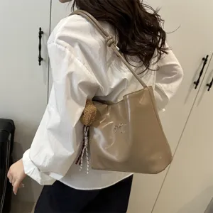 Detailed view of glossy khaki shoulder bucket bag with chic bow and cute bear charm.