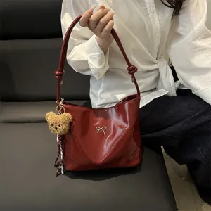 Chic wine red shiny shoulder bag for women, stylish minimalist faux leather bucket bag with bear charm.