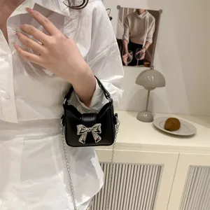 Detailed shot of a chic black mini handbag featuring a shiny silver bow and chain strap.