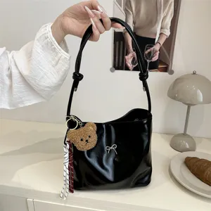Black glossy shoulder bucket bag detail view with cute plush bear keychain and knot strap.