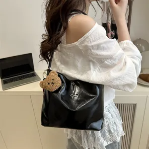 Black patent leather shoulder bucket bag with cute teddy bear pendant and metal bow detail.