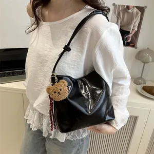 Black glossy underarm shoulder bucket bag with cute plush bear and bow accessory for women.