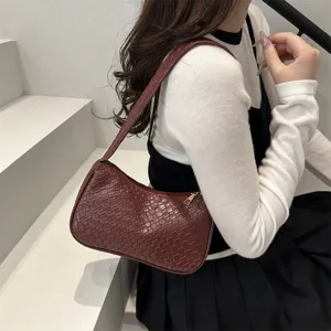 Close-up of a stylish dark red woven leather shoulder bag worn on the arm, indoor staircase setting.
