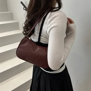 Detail shot of women's wine red textured leather underarm shoulder bag worn on model.