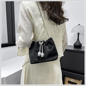 Detail shot of stylish black bucket bag with chain strap and drawstring design in indoor setting.