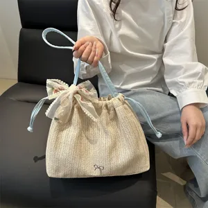 Detail view of stylish straw bucket bag with blue handle, floral lace bow, and spacious design.