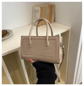 Detail view of minimalist beige leather tote handbag with dual handles and crossbody strap.