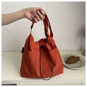 Orangefarbene Schultertasche mit vielen Taschen, Kordelzug und modischem Crossover-Design.