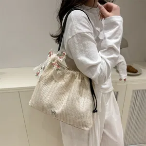 Detailed view of beige woven straw tote bag with delicate floral lace ribbon and black handles.