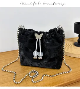 Stylish black velvet bucket bag featuring a metal chain strap and cute butterfly charm detail.