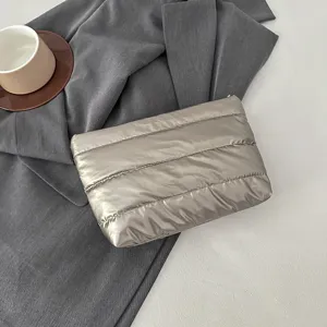 Close-up detail of silver padded clutch bag, sleek quilted puffer design, elegant fabric texture.