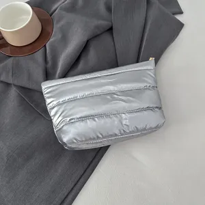 Silver puffer cosmetic clutch bag detail view, soft quilted fabric pouch with zipper closure.