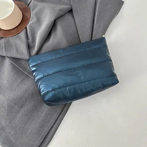 Detailed shot of quilted puffy clutch bag in dark blue, soft fabric texture and neat stitching.