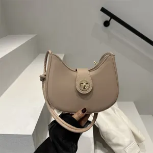 Close-up of beige dumpling underarm bag with gold lock detail in minimalist setting