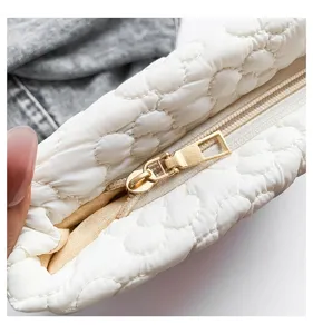 White quilted cosmetic bag detail shot showing gold zipper texture and soft puffy fabric design.