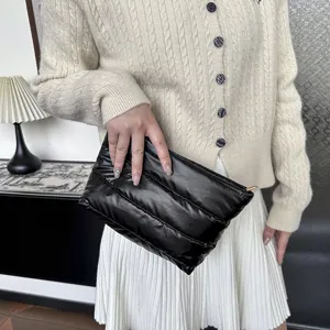 Detailed view of the black quilted puffer clutch bag, showing soft texture and metal zipper.