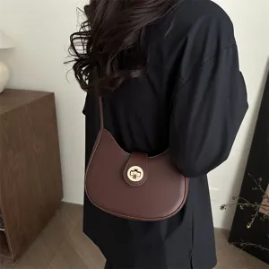 Detail view of a stylish brown crescent shoulder bag featuring gold turn-lock closure.