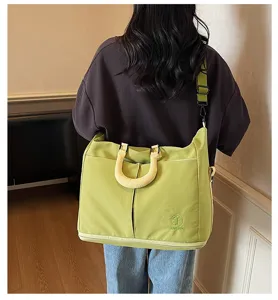 Detail view of large capacity green canvas travel shoulder bag with yellow handles and strap.