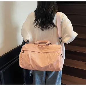 Pink travel duffel bag detail showcasing geometric texture, dual handles and adjustable shoulder strap.