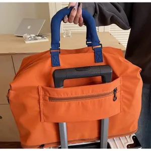 Detail view of large capacity orange travel duffel bag with luggage sleeve and blue handle.