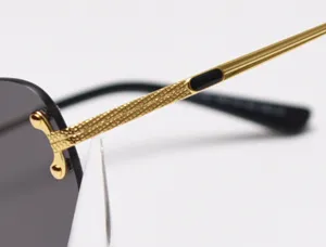Luxury rimless sunglasses detail showcasing gold textured metal temple and gradient dark lens design.