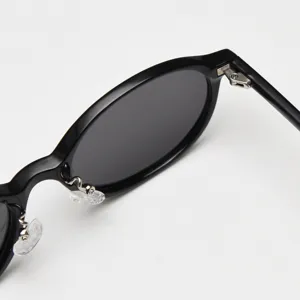 Close-up detail of black oval sunglasses frame, featuring metal hinge and clear nose pads.