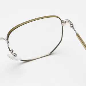Dettaglio montatura occhiali in metallo poligonale, design chic verde oliva e argento.