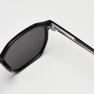 Gros plan de lunettes de soleil, monture en acétate noir avec charnière et branche.