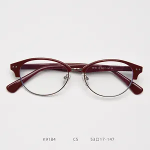 Primo piano della montatura per occhiali rossa in acetato, bordo metallico ovale, elegante.
