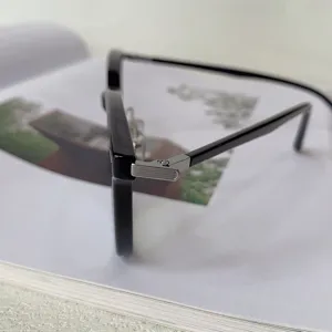 Close-up detail of black optical glasses frame with stylish metal hinge on white book.