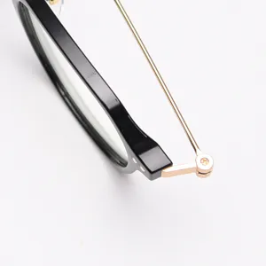 Close-up detail of stylish black frame glasses with fine gold metal temples and hinge structure.
