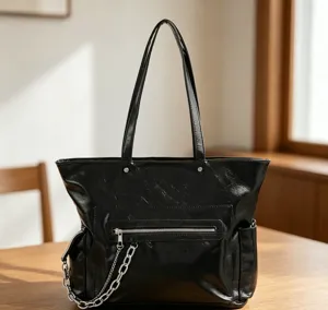 Vue détaillée du sac cabas en cuir noir brillant avec poche zippée avant et chaîne métallique.