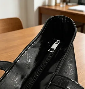 Gros plan sur la fermeture éclair du cabas vernis noir, sac à main minimaliste chic.