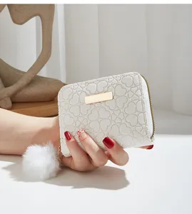 White short wallet detail showcasing embossed clover texture, gold metal plate and plush charm.