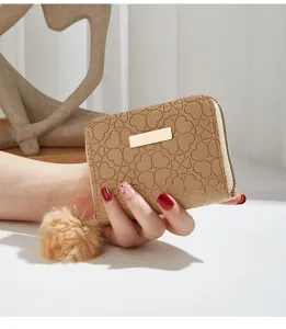 Detail shot of beige short zip coin purse with cute heart embossed pattern and fluffy pom pom charm.