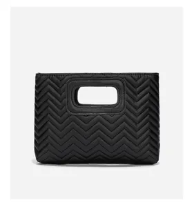 Black quilted zigzag clutch bag with cut-out handle, minimalist fashion commuter handbag detail.