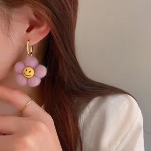 Purple plush flower earrings detail shot featuring cute yellow smiley face and gold hardware.