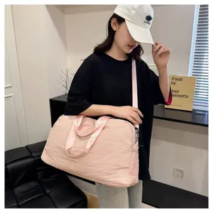 Detailed view of a light pink travel duffle bag worn by a model in a clean indoor setting.