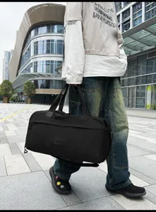 Outdoor street detail view of a large capacity black travel duffel bag with model present.