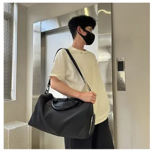 Detail shot of a black nylon travel duffel bag carried by a model in a modern indoor setting.