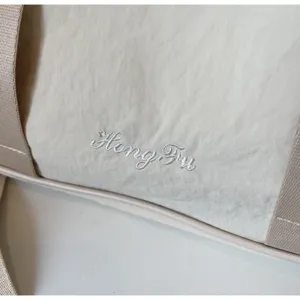 Close-up of beige oxford fitness travel bag, showing delicate embroidery details and wide strap.