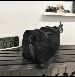 Detail view of black gym duffel bag with side mesh pocket and sturdy shoulder strap.
