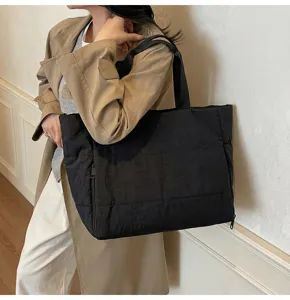 Black quilted tote bag detail shot showing large capacity design and side zipper pocket.