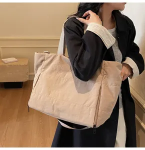 Detail shot of the large beige canvas tote bag worn by a model in a minimal room.
